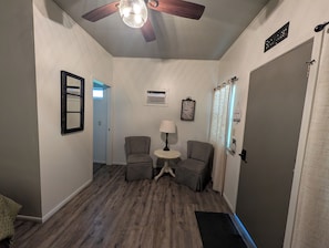 A hallway with a ceiling fan, a wall-mounted air conditioner, a clock, and a door with a sign above it.
