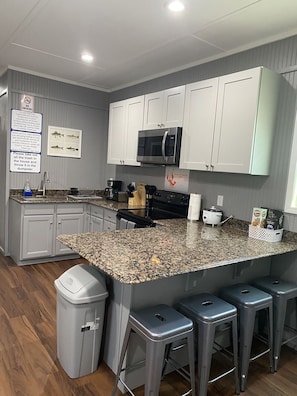 A kitchen with white cabinets, a granite countertop, a stainless steel microwave, and a trash can. - Blue crab house boat, Wi-Fi, Ice machine, sleeps 8,perfect place to fish (Venice)