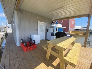 A covered outdoor area with a wooden deck, a table, and a white refrigerator. - Blue crab house boat, Wi-Fi, Ice machine, sleeps 8,perfect place to fish (Venice)