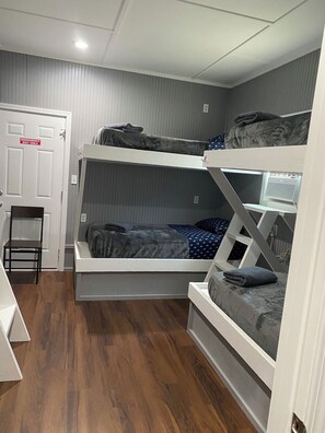Habitación con literas, una silla y una puerta que indica 'Salida de Emergencia Únicamente'.
