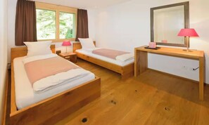A hotel room with two single beds, a desk, a mirror, and a window with curtains. - DESIGNED TO COMBINE CONTEMPORARY COMFORT WITH THE CHARM OF SWISS ALPS-ZERMATT (Zermatt)