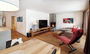 A modern living room with a flat-screen TV, a stone fireplace, a red chair, and a sofa. - DESIGNED TO COMBINE CONTEMPORARY COMFORT WITH THE CHARM OF SWISS ALPS-ZERMATT (Zermatt)
