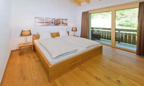 A bedroom with a wooden bed, two bedside tables with lamps, a large window with a view of greenery, and a wall with three framed pictures. - DESIGNED TO COMBINE CONTEMPORARY COMFORT WITH THE CHARM OF SWISS ALPS-ZERMATT (Zermatt)