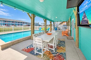 A covered outdoor area with a pool, white furniture, and a colorful rug. - Coastal Escape | Private Pool + Games | Sleeps 12 (Port Aransas)