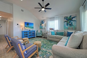 A living room with a ceiling fan, a blue cabinet, a sofa, and a coffee table. - Coastal Escape | Private Pool + Games | Sleeps 12 (Port Aransas)