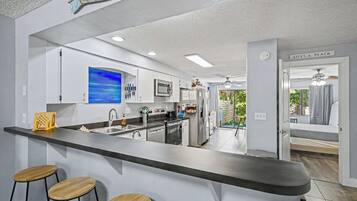 Une cuisine moderne avec un coin bar, des appareils en acier inoxydable et une vue sur une chambre à coucher.