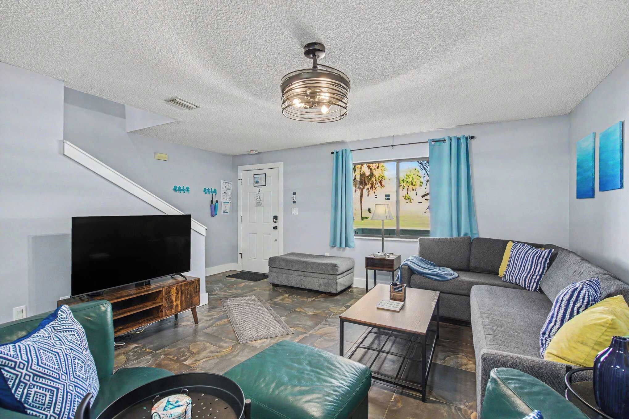 A modern living room with a flat-screen TV, a sofa, a coffee table, and a patterned rug.
