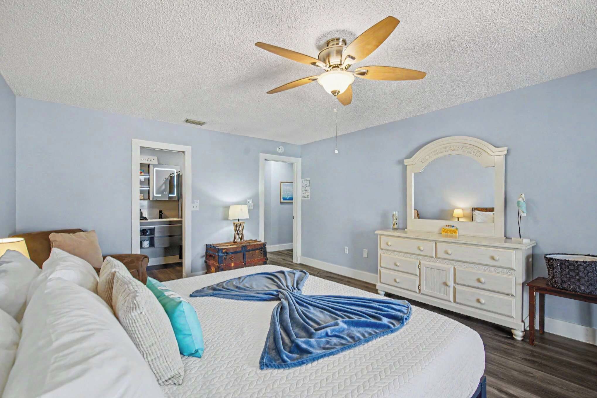 A bedroom with a bed, a dresser, a mirror, a ceiling fan, and a walk-in closet.
