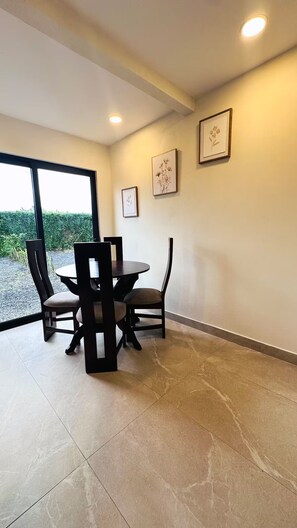 A dining area with a round table and chairs, framed artwork on the wall, and a view through a glass door. - Sapphire House (La Perla)