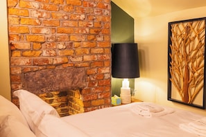 Ein Hotelzimmer mit Kamin aus Backsteinen, einem Bett mit weißen Leinen, einer schwarzen Lampe und einem Wandbild.
