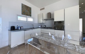 Una cocina moderna con armarios blancos, una mesa de comedor de vidrio y una campana extractora de acero inoxidable.