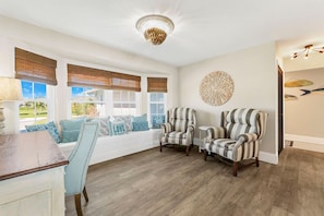 A room with a large window, two armchairs, a bench with cushions, and a decorative wall piece. - Schell-Nanigans Lake Front Sunrise (Cape Coral)