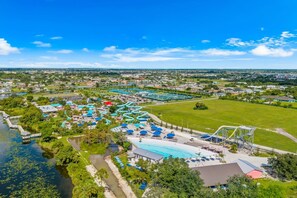 An aerial view of a resort with a large swimming pool, water slides, and a dock extending into a body of water. - Schell-Nanigans Lake Front Sunrise (Cape Coral)