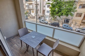 A balcony with a table and chairs, overlooking a street with parked cars and buildings. - Sunny 1BR Apartment in Pietà with Balcony (Tal-Pietà)