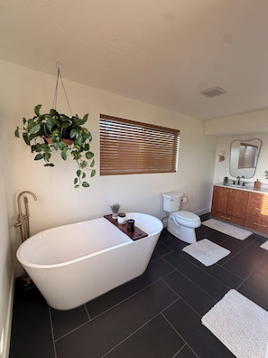 A bathroom with a freestanding bathtub, a toilet, a sink with a mirror, and a hanging plant. - 4-bedroom House in Prime SLC Location Minutes From The U (Salt Lake City)