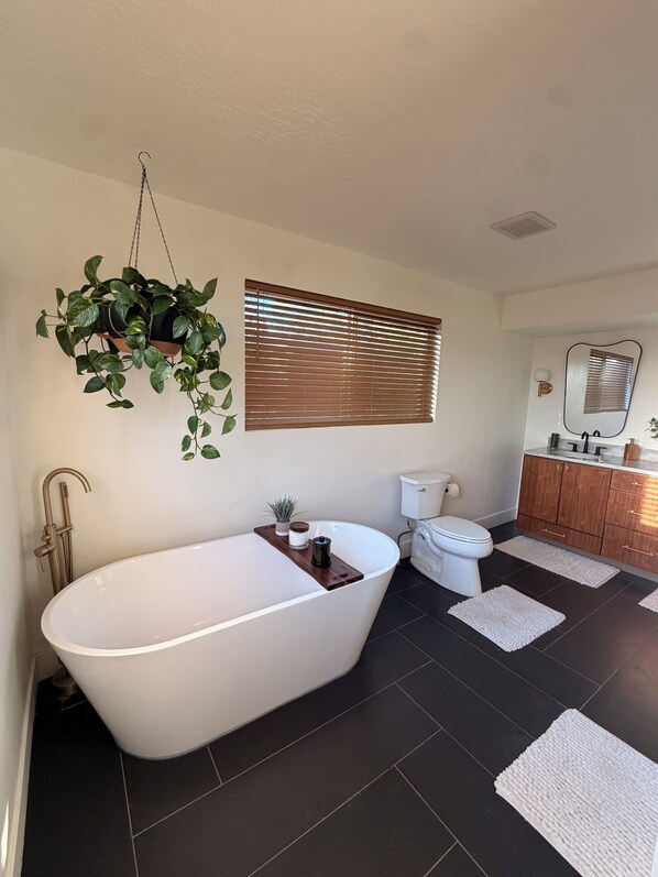 A bathroom with a freestanding bathtub, a toilet, a sink with a mirror, and a hanging plant. - 4-bedroom House in Prime SLC Location Minutes From The U (Salt Lake City)