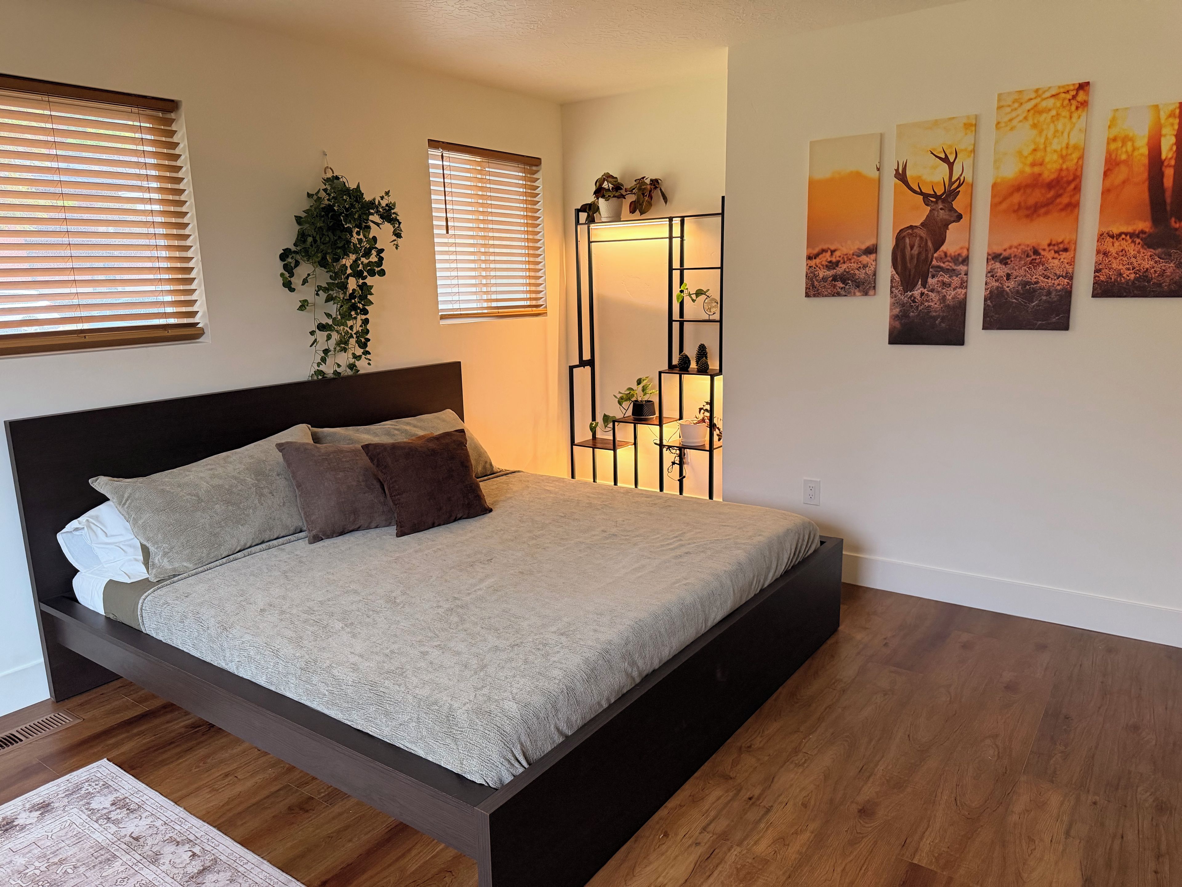 Un dormitorio con una cama, una planta en la mesita de noche, una estantería con plantas y decoración en la pared.