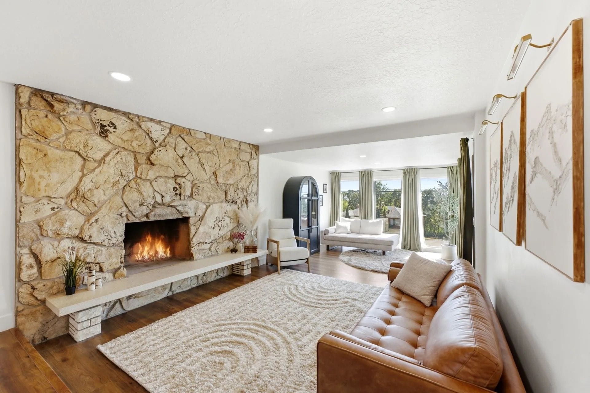 A modern living room with a stone fireplace, a leather sofa, and a large window offering a view of the outdoors.