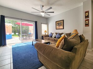 A living room with a sofa, a coffee table, a ceiling fan, and a sliding glass door leading to an outdoor patio area. - Charming 3-bedroom townhome with AC in fantastic Kissimmee (Kissimmee)