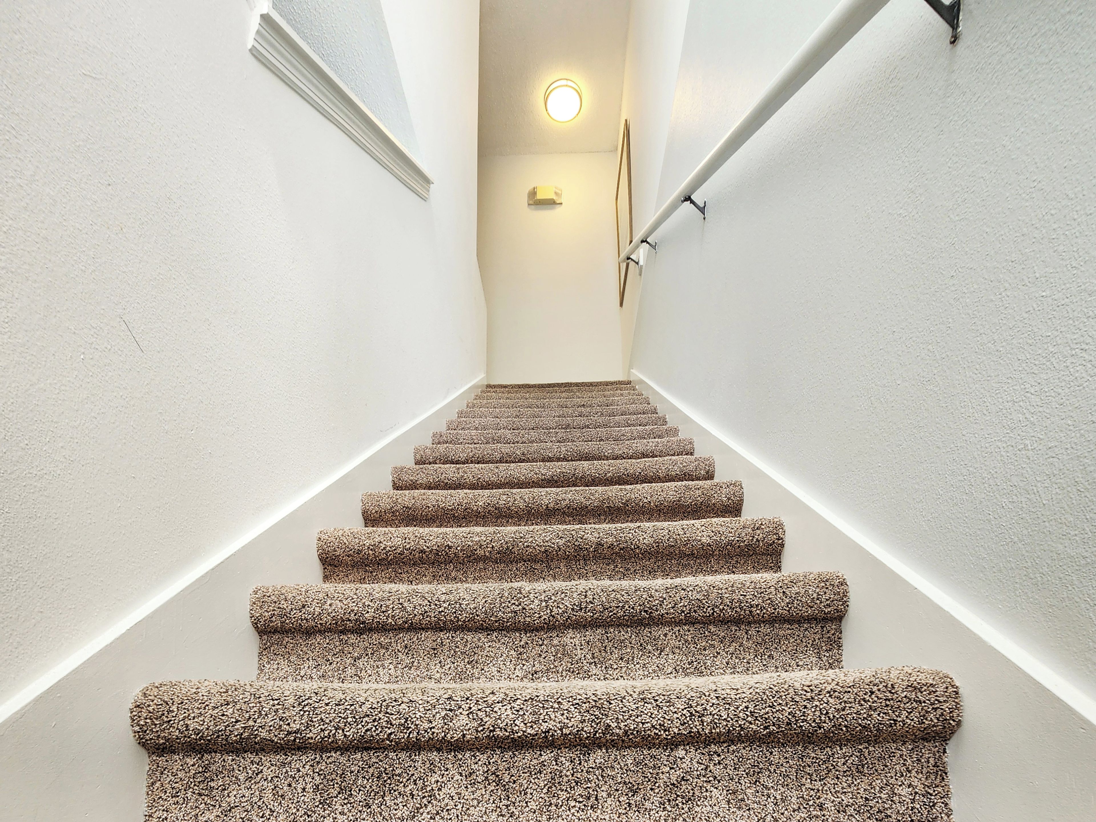 Een betegelde trap met een leuning, een wandlamp en een raam aan de linkerkant.
