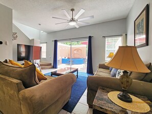 A living room with a ceiling fan, a flat-screen TV, a sofa, a coffee table, and a lamp. - Charming 3-bedroom townhome with AC in fantastic Kissimmee (Kissimmee)