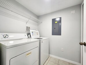 Une buanderie équipée d’un lave-linge et d’un sèche-linge à chargement frontal, d’une bouche d’aération au-dessus du sèche-linge et d’une porte donnant sur la pièce technique.