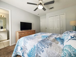 Une chambre à coucher avec un lit, un téléviseur posé sur une commode, un ventilateur de plafond et une porte.