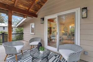 Eine überdachte Terrasse mit zwei gemusterten Stühlen, einem Glastisch und einem Blumentopf.