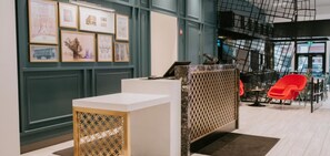 Un espace d’accueil avec un comptoir de réception blanc, des œuvres d’art encadrées accrochées au mur et un fauteuil rouge.