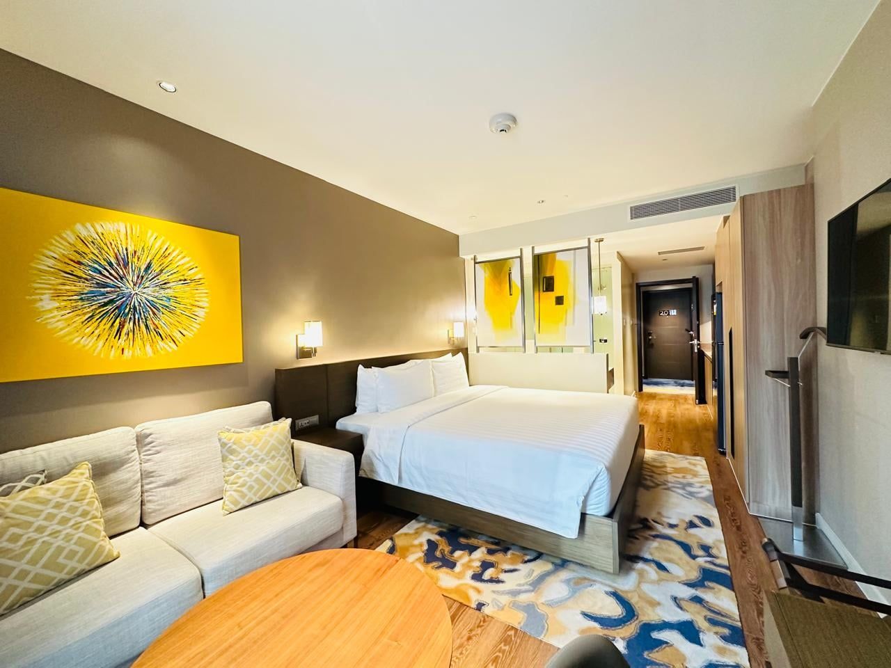 A hotel room with a bed, a sofa, a coffee table, and a painting on the wall.