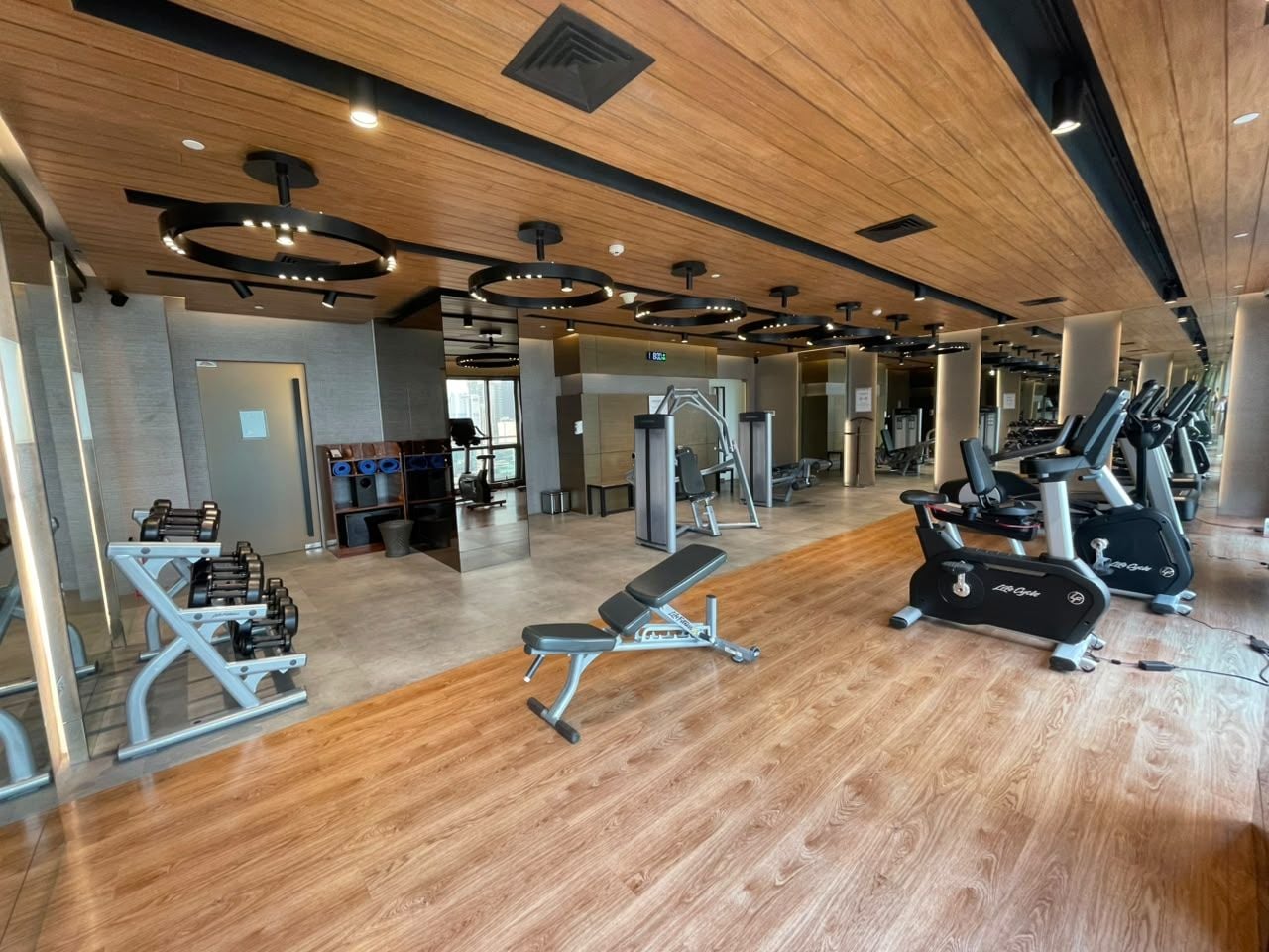 A gym with exercise equipment, wooden flooring, and a modern ceiling design.