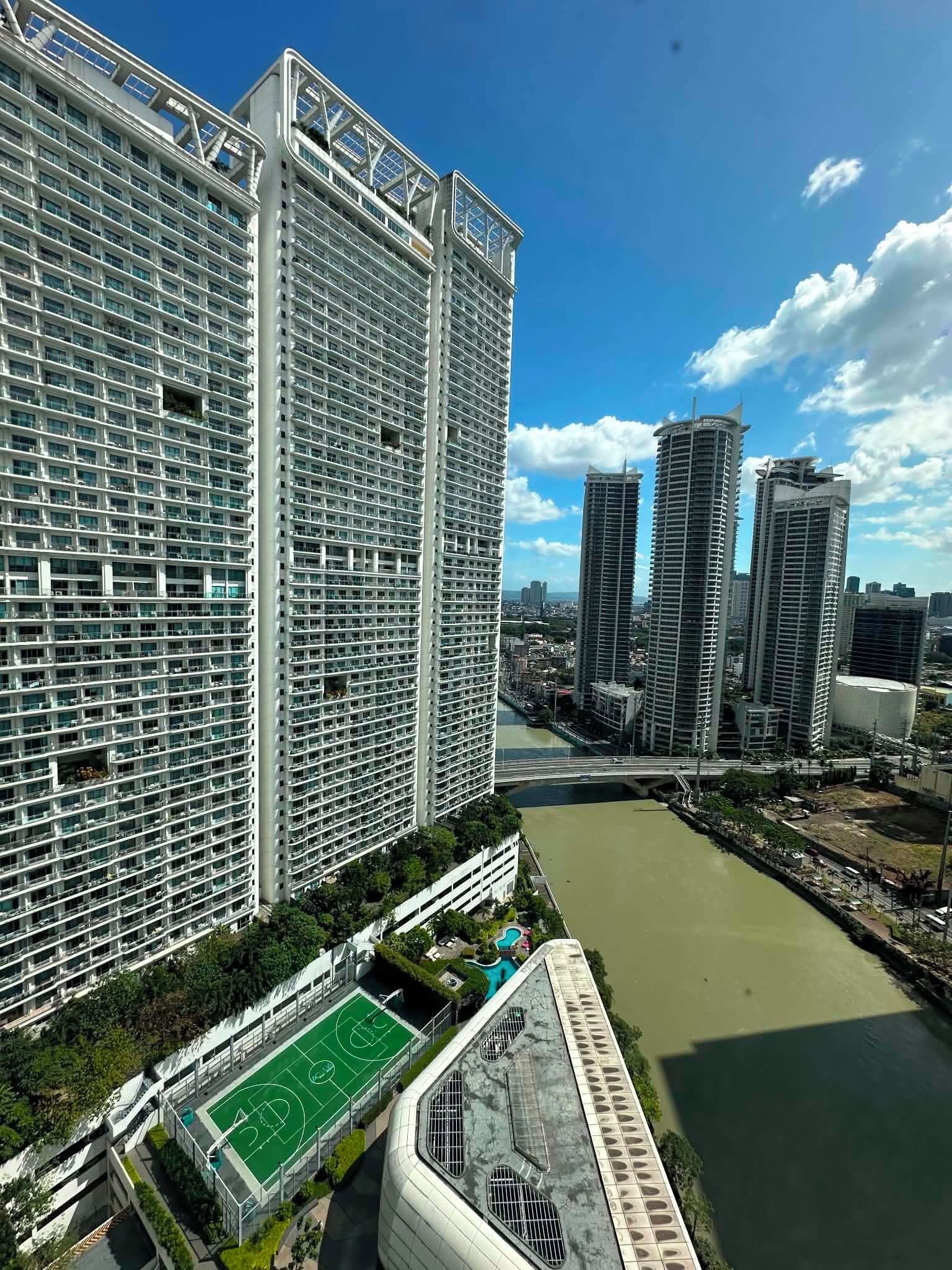 A high-rise building with a grid of windows, a river, and a bridge in the background.