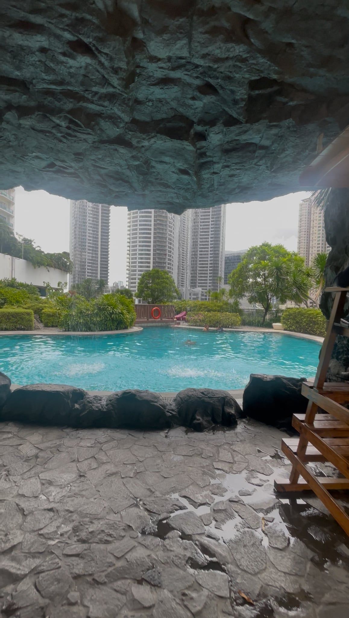 A swimming pool with a rocky foreground and a view of high-rise buildings in the background.