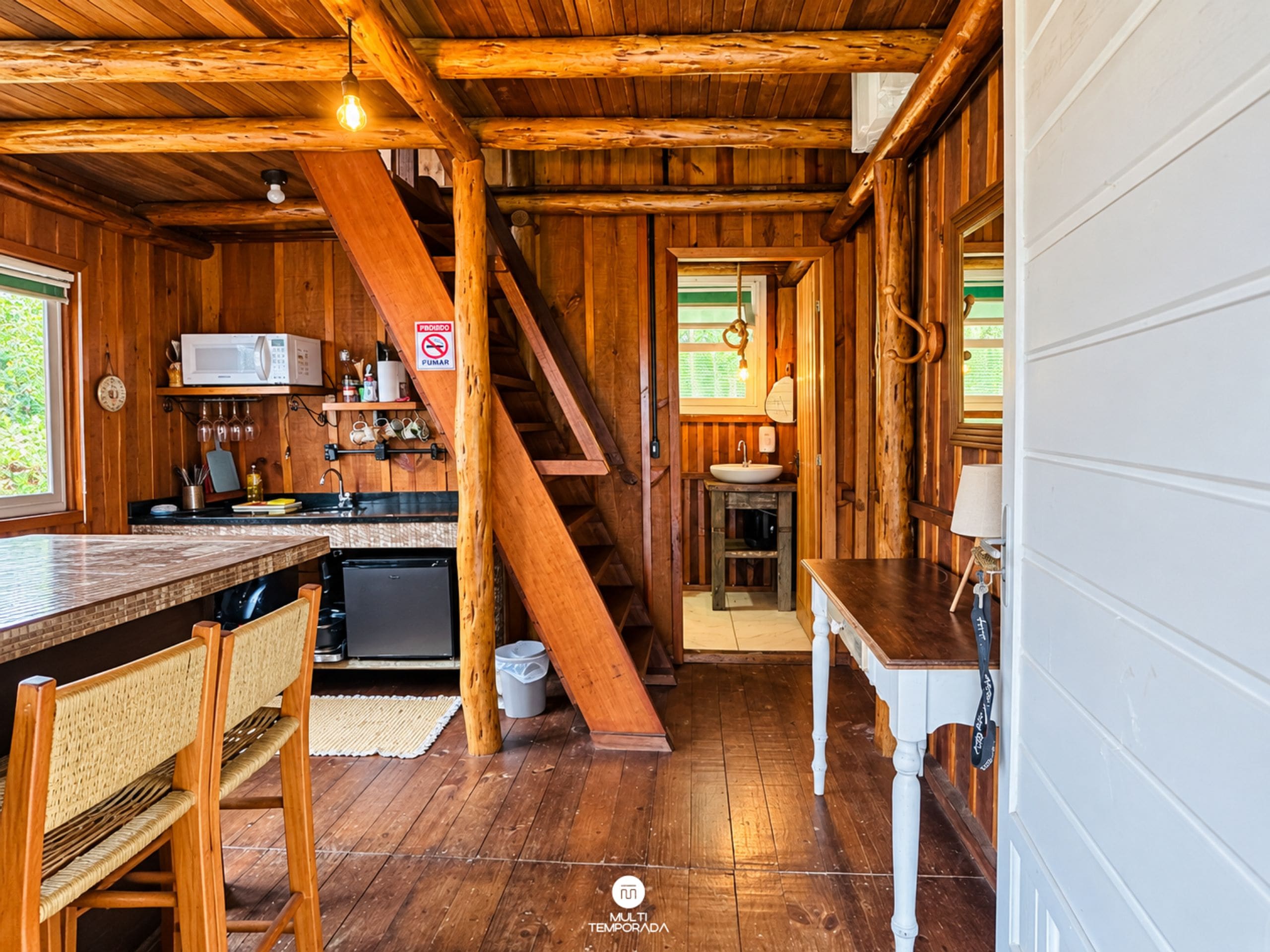A wooden cabin interior with a kitchen, dining area, and a staircase.