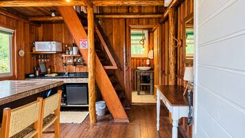 A wooden cabin interior with a kitchen, dining area, and a staircase.