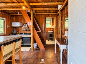 A wooden cabin interior with a kitchen, dining area, and a staircase.