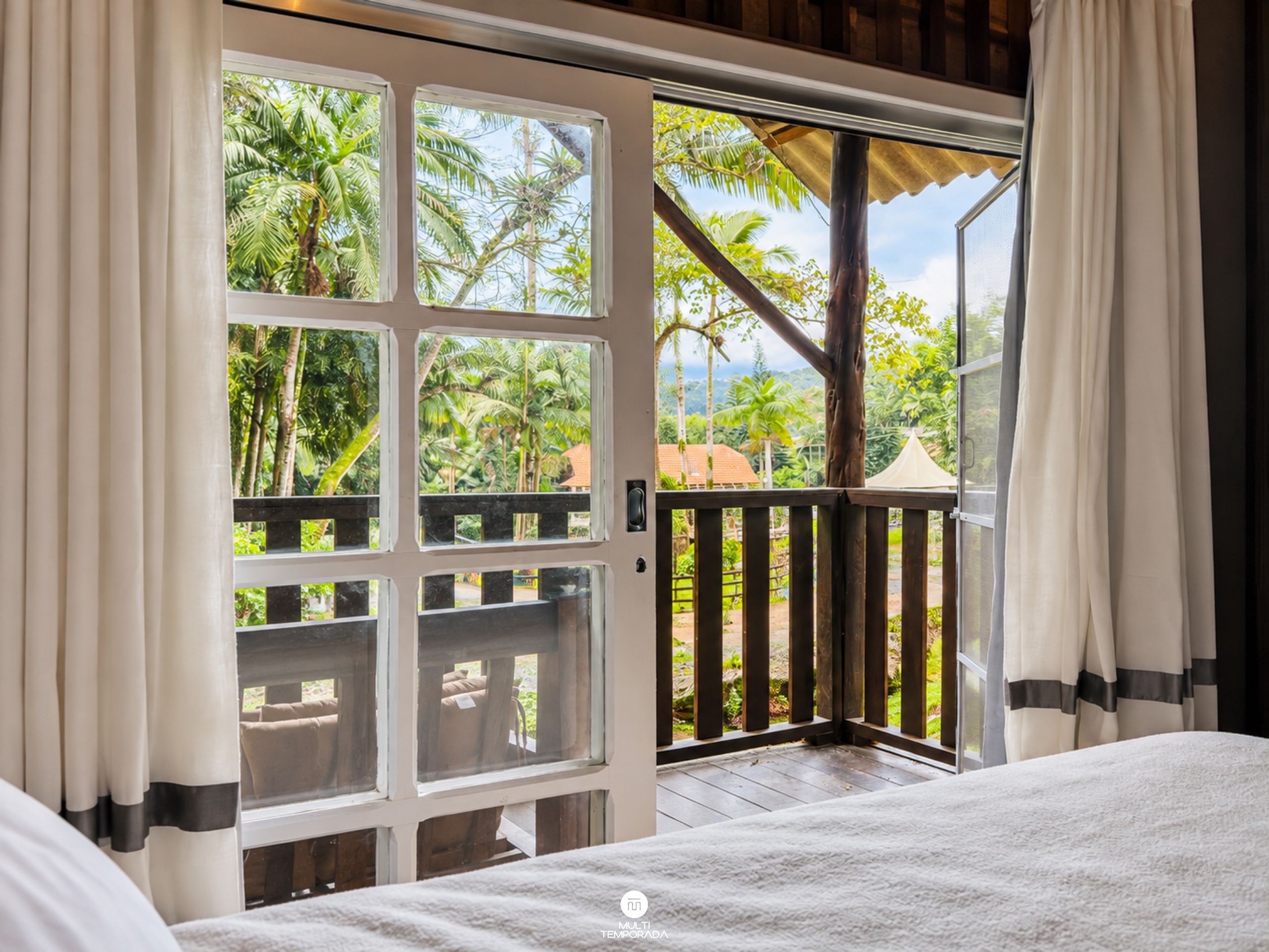 Una habitación con un amplio ventanal corredera que da a un espacio exterior con terraza de madera y vistas a palmeras.