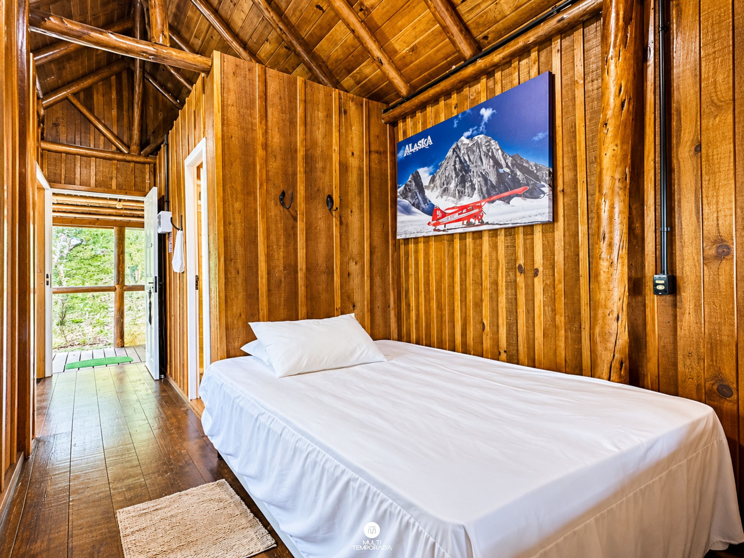 A wooden cabin room with a bed, a wooden ceiling, and a poster of a mountain.