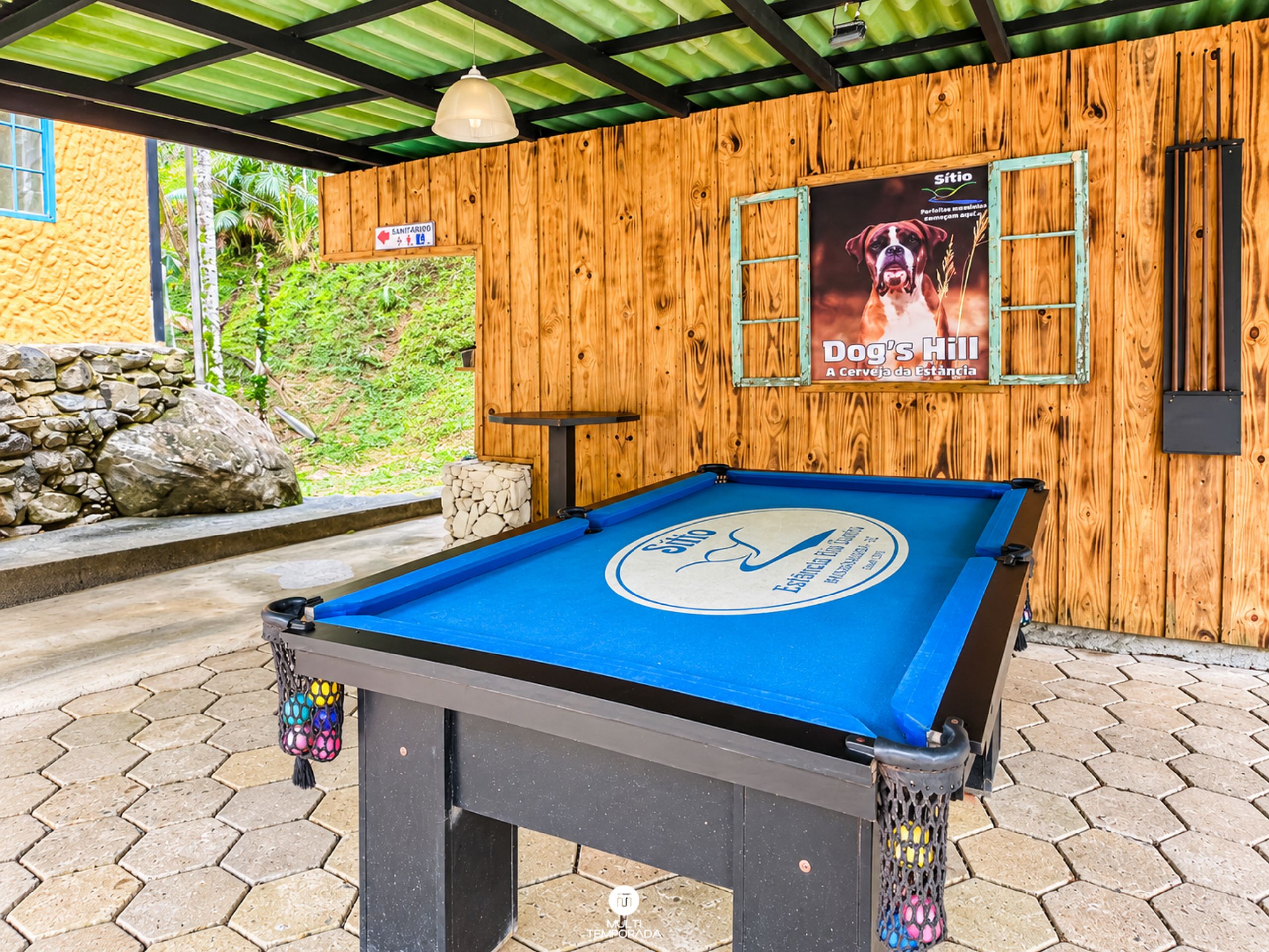 A pool table with a logo, a wooden wall with a poster, and a stone wall with a sign.