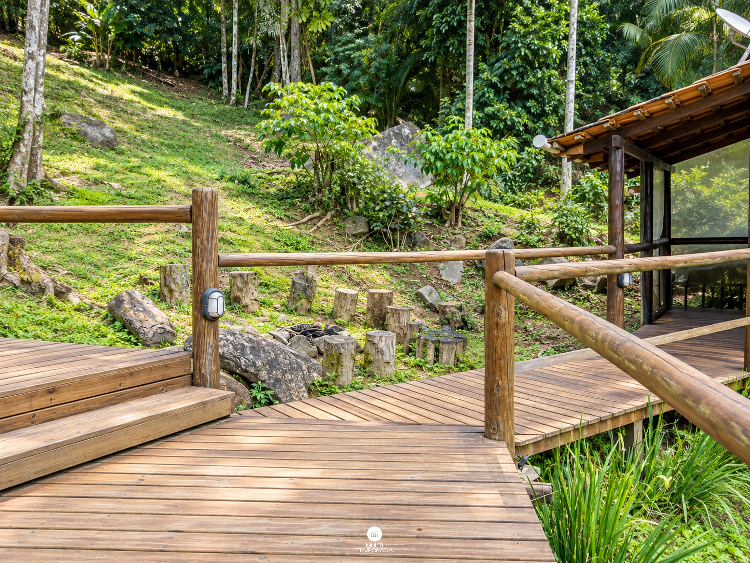 Una terraza de madera con barandilla, rodeada de abundante vegetación y rocas.