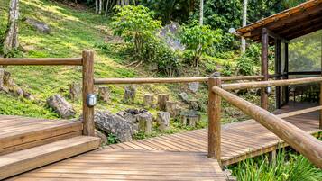 Una terraza de madera con barandilla, rodeada de abundante vegetación y rocas.