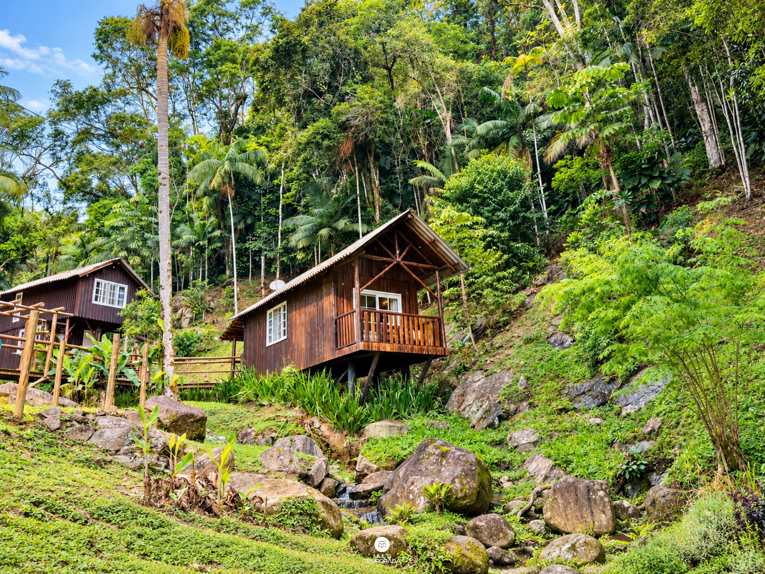 Une cabane en bois dotée d’un balcon, entourée d’une végétation luxuriante et de rochers.