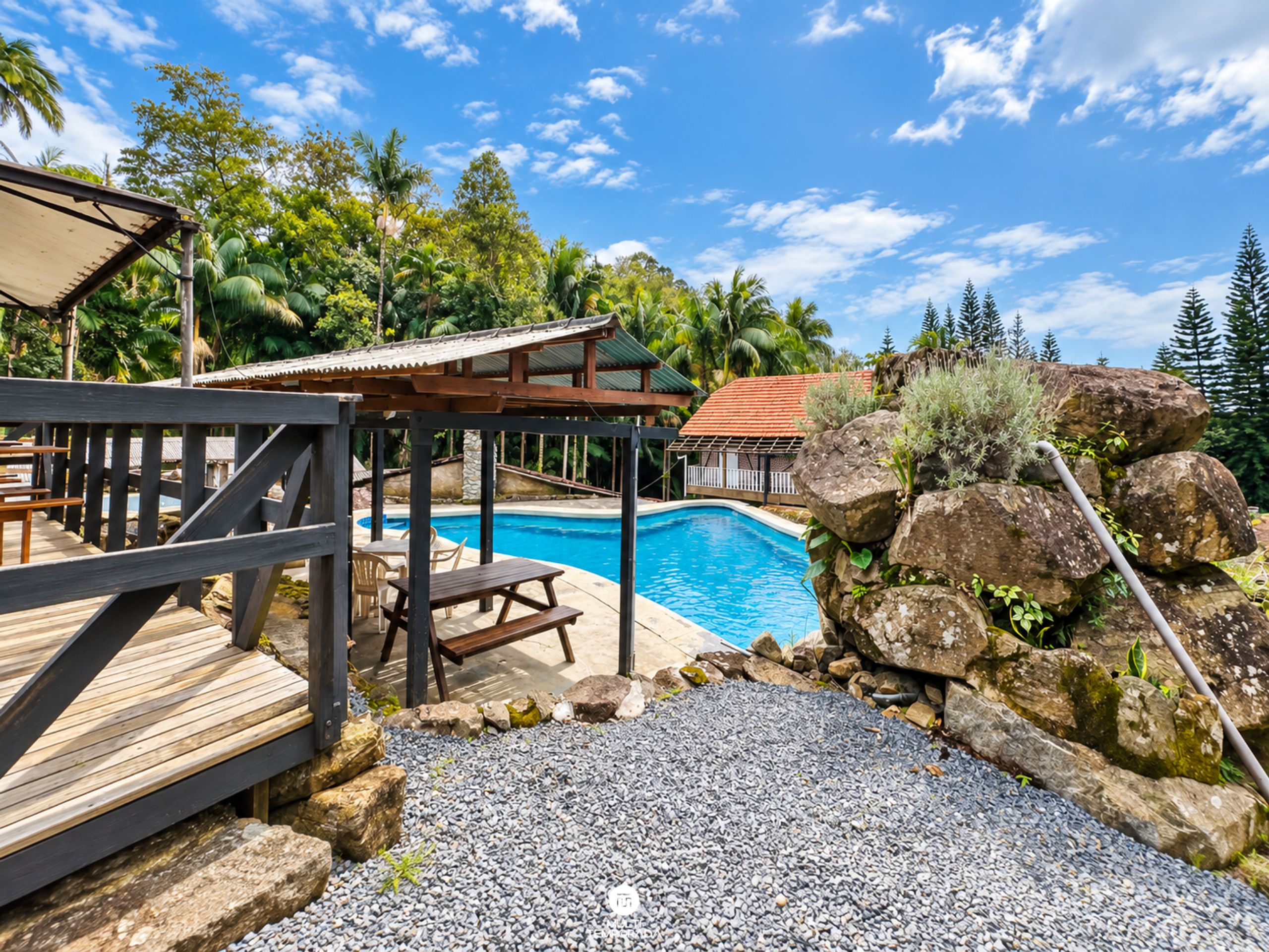 Un espace piscine doté d’une terrasse en bois, de tables de pique-nique et offrant une vue sur un paysage tropical.