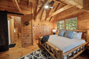 A wooden cabin bedroom with a bed, a nightstand, a lamp, and a window. - The Nook - Mountain Views - Hot tub  - Dogs  - Hiking (Blue Ridge)