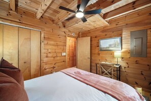Een kamer met houten vloeren, een bed, een plafondventilator, een bureau en een stoel.