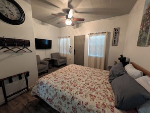 A bedroom with a bed, a chair, a TV, a ceiling fan, and a coat rack. - Sweet Mountain Cabin at Clingan's Junction Cabins & Coffee (Yokuts Valley)