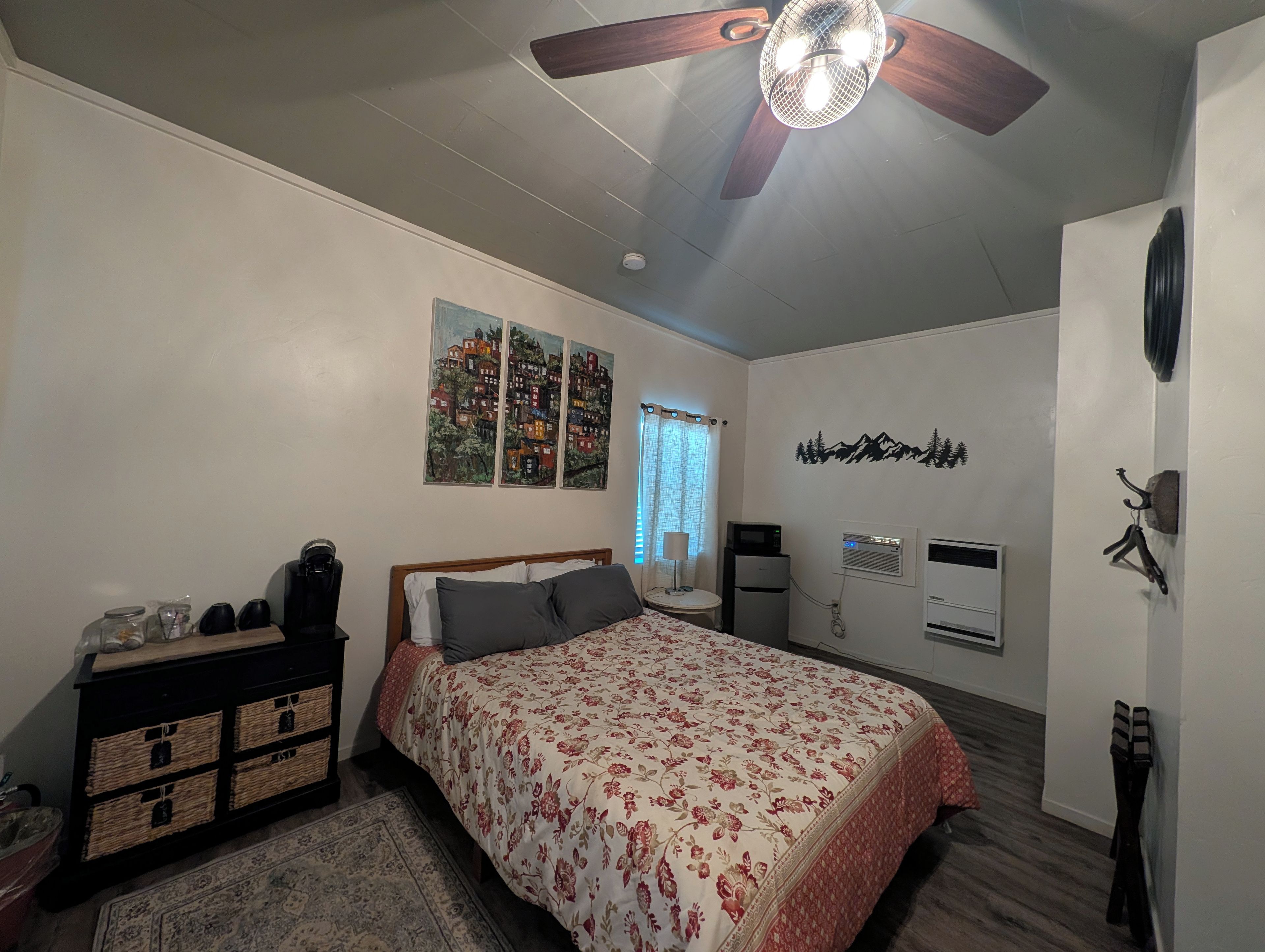 Un dormitorio con cama, ventilador de techo, calefactor de pared, radiador y pared decorada con motivos de montaña.