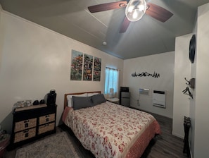 A bedroom with a bed, a ceiling fan, a wall-mounted heater, a radiator, and a wall with a mountain decoration.
