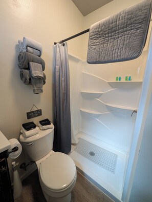 Een badkamer met een toilet, een douche met een grijs douchegordijn en een handdoekrek met opgevouwen handdoeken.