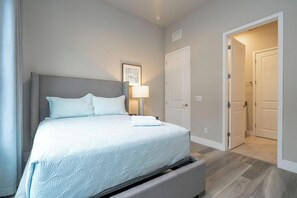 Une chambre à coucher comprenant un lit, une table de chevet, une lampe et une porte donnant sur une autre pièce.